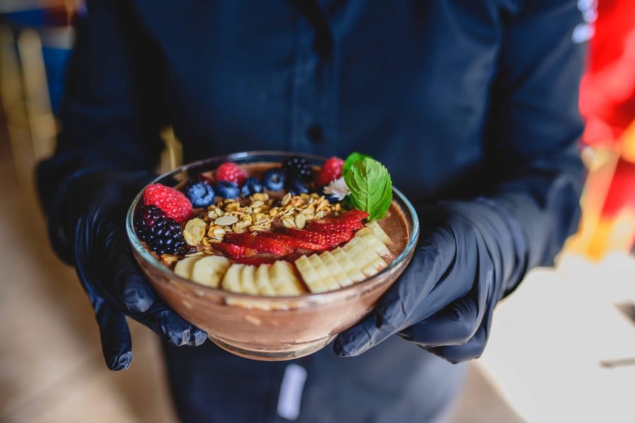 An acai bowl topped with berries, banana and granola, handed over the counter